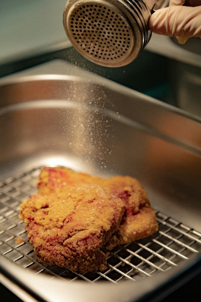 Golden fried chicken being seasoned fresh in the deli kitchen