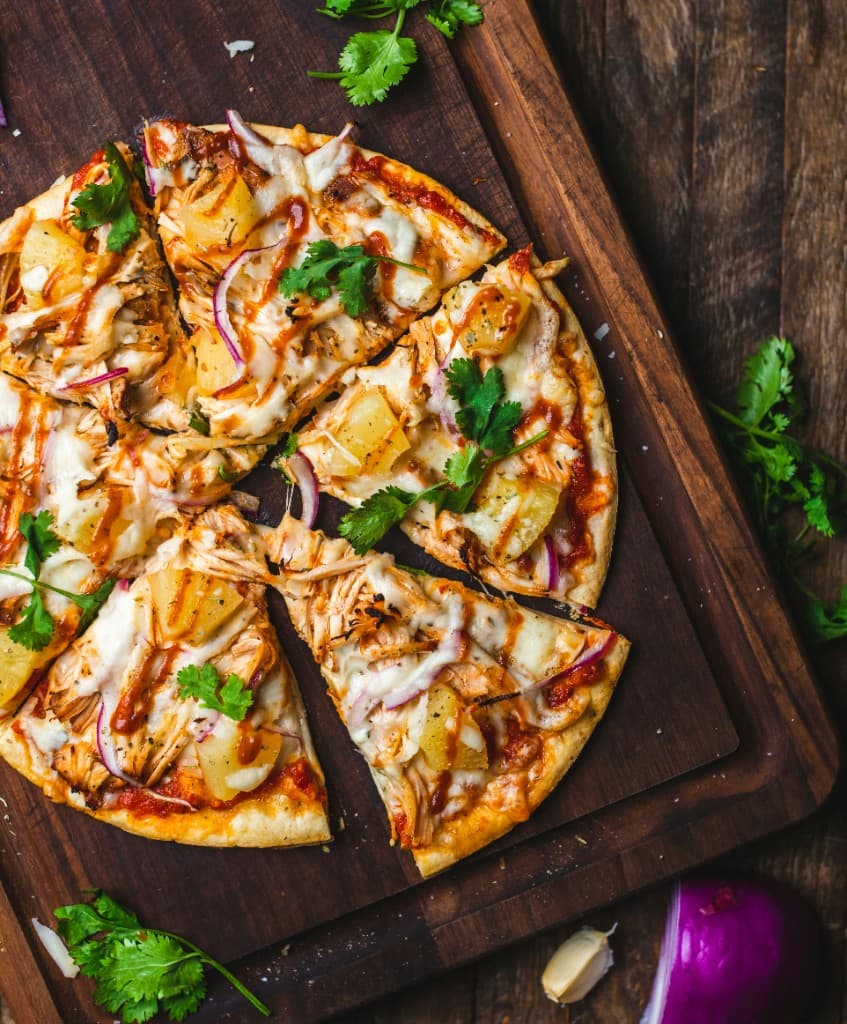 BBQ chicken pizza with pineapple, red onion, and cilantro on a wooden board